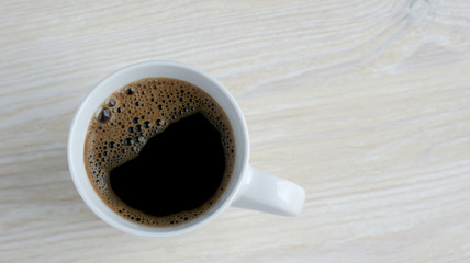 delicious fragrant black coffee with foam in a White mug on a wooden table in the morning on a Sunny day, which helps to cheer up