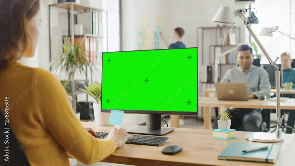 Aufkleber over the shoulder: creative young woman sitting at her desk using desktop computer with mock-up gree