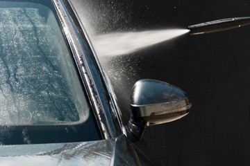 Сar washing with high pressure water jet. Water and foam under pressure flies toward the car body. Close-up view