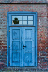 Old blue rusted door in industrial area against light colored brick wall