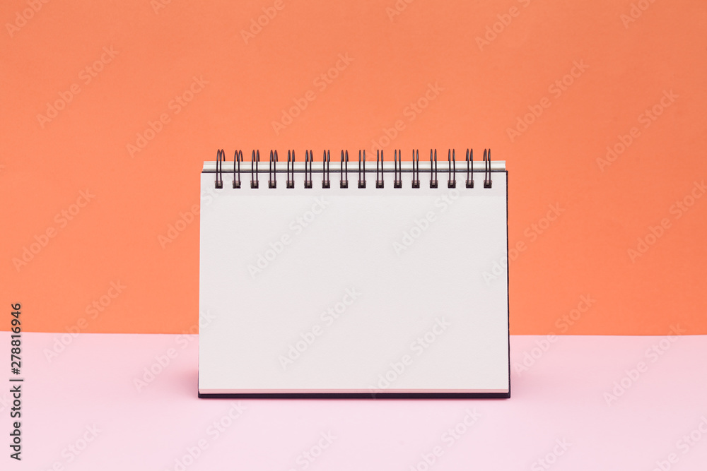 Wall mural blank sketchbook or calendar concept on colored background. empty notepad on pink and orange backgro