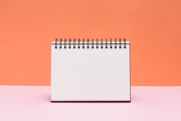 Blank sketchbook or calendar concept on colored background. Empty notepad on pink and orange background.