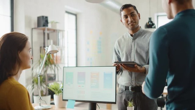 Three Mobile Software Developers Work on Desktop Computer, They Discuss Smartphone Application Design Use Touch Screen Digital Tablet. Modern Stylish Office with Diverse Team of Professionals Working