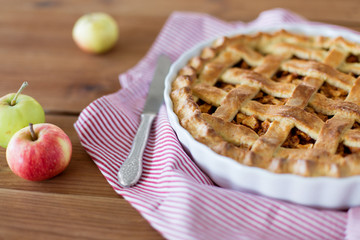 food, culinary and eating concept - close up of apple pie in baking mold with knife on kitchen towel