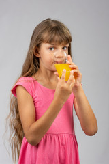 The girl drinks orange juice from a glass and looks at the frame