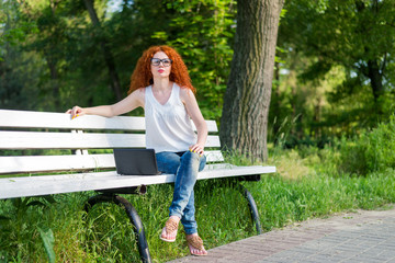 Naklejka premium Red-haired female freelancer working on a laptop while sitting on a park bench.