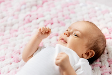 babyhood and people concept - sweet little baby girl lying on knitted pink blanket of plush yarn
