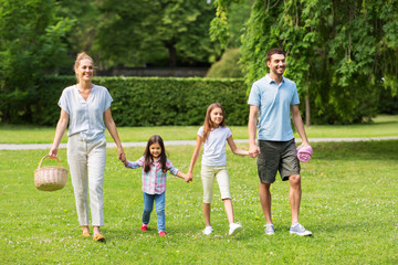 family, leisure and people concept - happy mother with picnic basket, father and two daughters walking in summer park