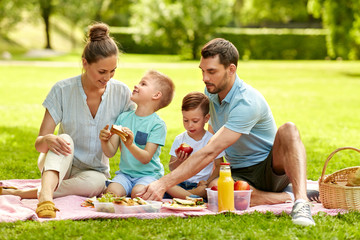 family, leisure and people concept - happy mother, father and two little sons having picnic at...