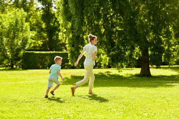 Naklejka na ściany i meble family, leisure and people concept - happy mother and little son running and playing catch game at summer park
