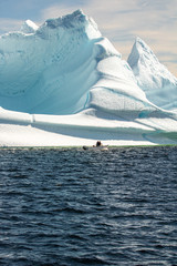 Naklejka premium A small boat sailing next to a massive iceberg floating off the coast of Twillingate Newfoundland, down 'iceberg alley'. 