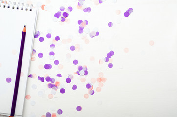 Notepad with confetti and colored pencils on the white background. Concept school supplies. Copy space, top view, flat lay