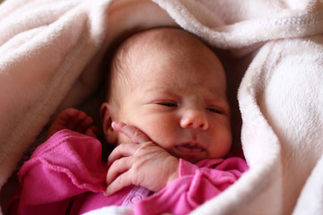 Cute sleeping newborn baby in pink baud on her bed under beige blanket.
