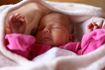 Cute newborn baby in pink baud is sleeping on her bed under beige blanket.