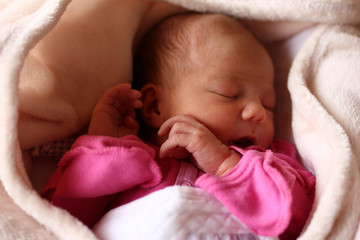 Cute sleeping newborn baby in pink baud on her bed under beige blanket.