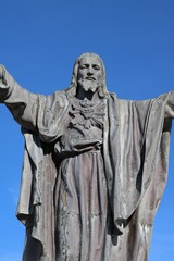 Closeup concrete statue of Jesus with thorn encircled heart isolated on blue sky