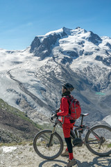 active senior woman, riding her electric mountainbikeon the Gornergrat in Zermatt, Wallis,Switzerland. In The background Gorner Glacier, Monte Rosa, Liskam am Breithorn