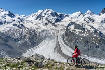 Fotobehang active senior woman, riding her electric mountainbikeon the Gornergrat in Zermatt, Wallis,Switzerland. In The background Gorner Glacier, Monte Rosa, Liskam am Breithorn © Uwe