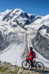 active senior woman, riding her electric mountainbikeon the Gornergrat in Zermatt, Wallis,Switzerland. In The background Gorner Glacier, Monte Rosa, Liskam am Breithorn