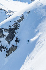 Skier drops into steep slope below granite cliff in the backcountry of Alaska's Talkeetna Mountains.
