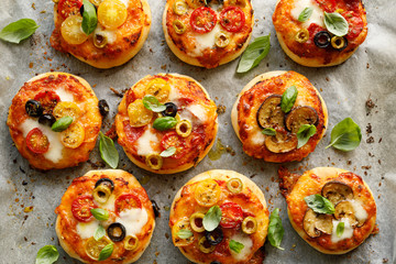 Mini vegetarian pizzas with the addition various kinds of vegetables , mozzarella cheese and fresh basil on a on white baking paper, close-up, top view.