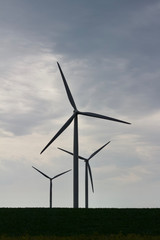 Fototapeta premium Silhouette of three giant wind turbines with a cloudy sky background
