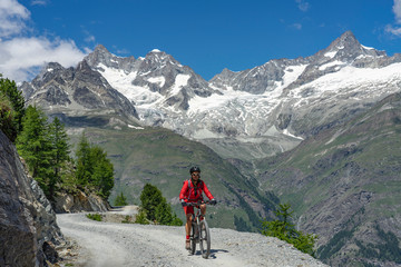 Fototapeta na wymiar active senior woman, riding her electric mountain bike below the Gornergrat in Zermat, Canton Valais, Switzerland, in The background Zinalrothorn and Obergabelhorn