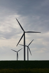 Silhouette of three giant wind turbines with a cloudy sky background