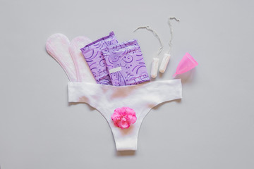White pants with medical female sanitary napkins, tampons, menstrual cup on white background. Concept of critical days, menstruation. Menstruation, means of protection