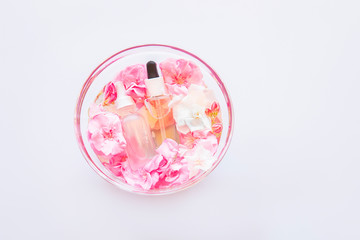 Group of skincare serum oil with little flowers in glass plate on white backdrop. Facial beauty cosmetic spa product. Natural cosmetology concept. Dropper of essential oil, aromatherapy essence