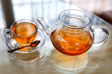 Transparent glass tea cup and pot with spoon on glass table in strong backlit