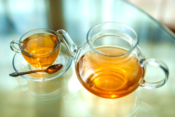 Transparent glass tea cup and pot with spoon on glass table in strong backlit