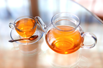 Transparent glass tea cup and pot with spoon on glass table in strong backlit