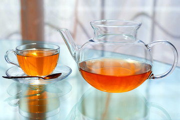 Transparent glass tea cup and pot with spoon on glass table in strong backlit