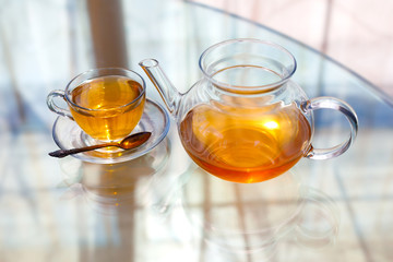 Transparent glass tea cup and pot with spoon on glass table in strong backlit