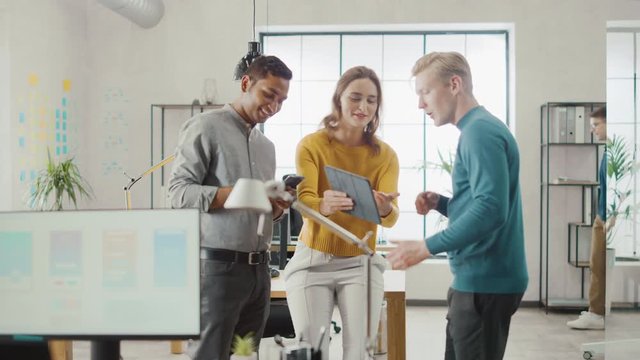 In the Office: Three Diverse Start-up Entrepreneurs Have Meeting and Discussion about the Project. Share Touch Screen Digital Tablet and Smartphone Screens.Young Professionals Smile and Joke Around
