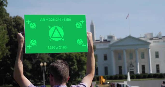 A man holds a blank green screen protest sign outside The White House in Washington, D.C. Tracking points included for custom sign message. The Washington Monument seen in the distance.  	