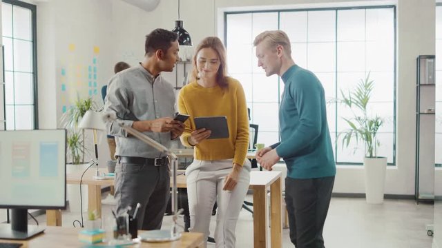 In the Office: Three Diverse Start-up Entrepreneurs Have Meeting and Discussion about the Project. Share Touch Screen Digital Tablet and Smartphone Screens.Young Professionals Smile and Joke Around