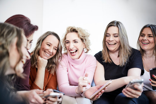 Group of six laughing women with smartphones