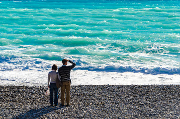 Couple standing on pebble beach looking out to sea.
