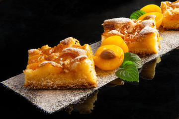 Pieces of plum cake with powdered sugar decorated with yellow plum and mint leaves on a dark...