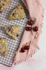 cherry and white chocolate scones on a black baking rack and pink marble background with a napkin and cherries vertical