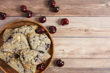 wood plate with cherry and white chocolate scones on a wooden table background with fresh cherries