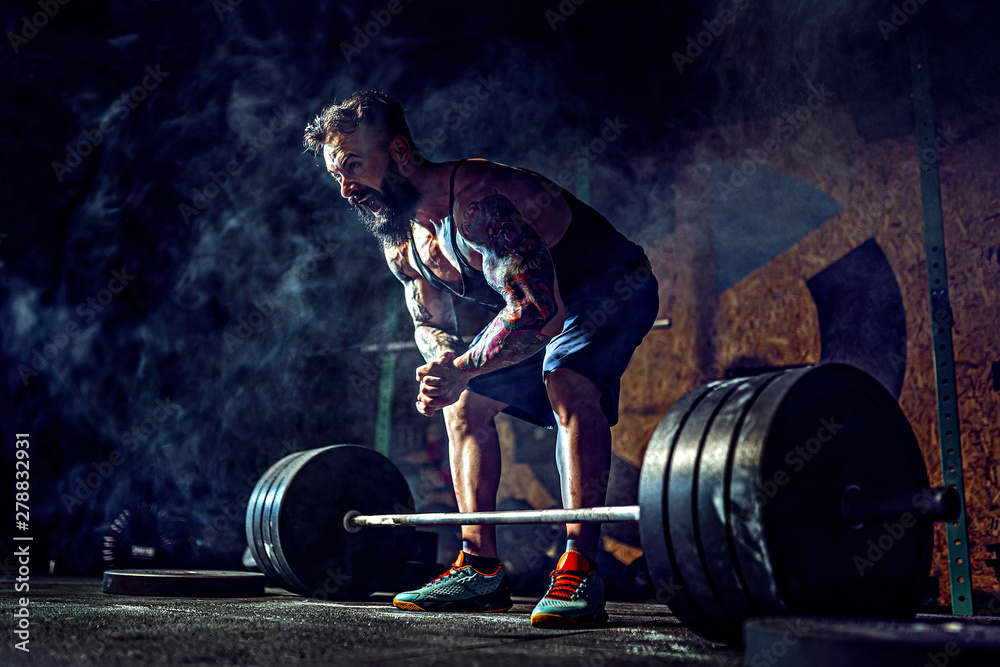 Wall mural muscular fitness man preparing to deadlift a barbell over his head in modern fitness center. functio