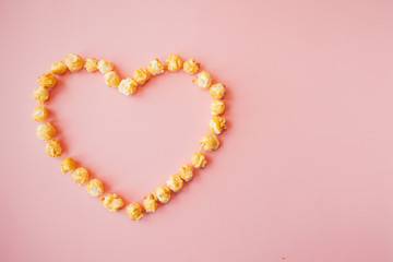 Love movies, concept on a pink background. Popcorn scattered on pink background heart shaped