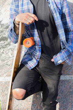 Tattooed young man with longboard leaning against wall, partial view