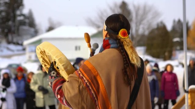 Environmentalists stage demonstration. A Native American plays music on a traditional drum, viewed from behind, during an outdoor gathering held by environmental campaigners.