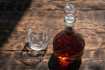 Strong alcohol in a transparent bottle and a drinking glass on a brown wooden table background.