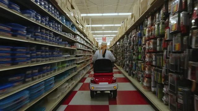 Woman with a disability in a electric mobility wheelchair scooter going in the merchandise rows in the supermarket mall. Disabled person independence concept. 4k.