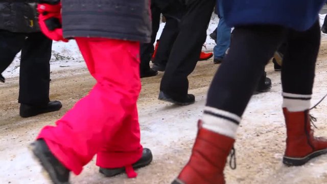 Activists march during ecological rally. Low angle footage on a group of protestors marching for planet earth. Legs of activists are seen marching past. A young child is pulled along the snow in a sle